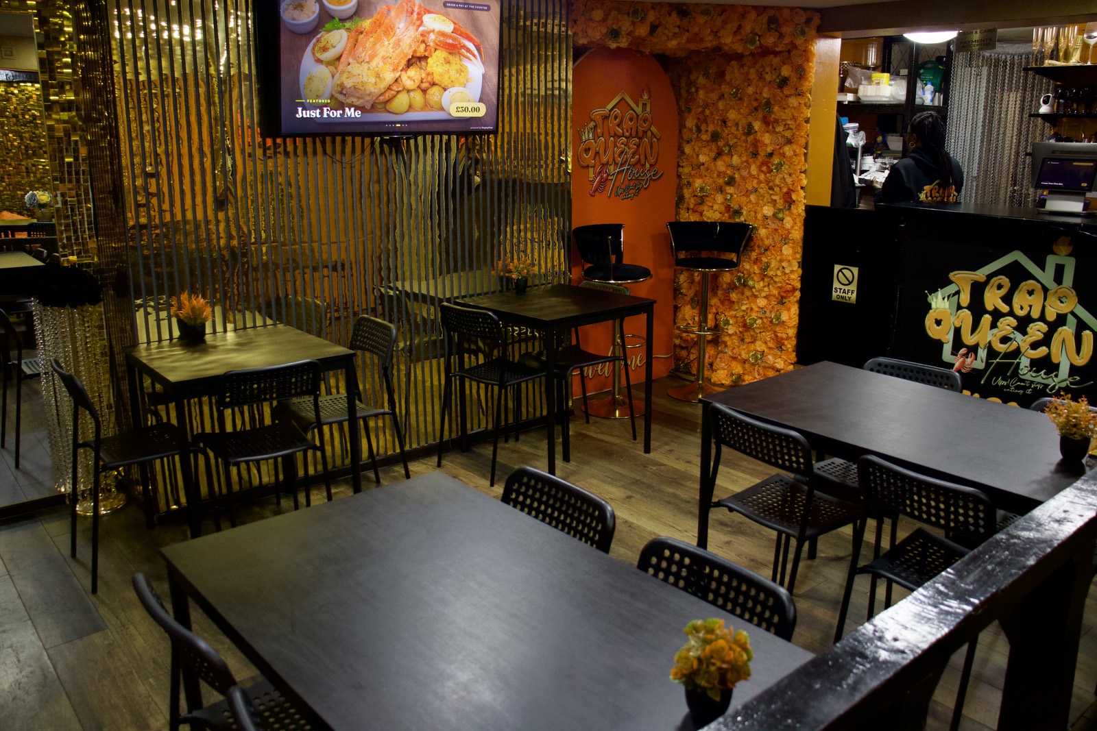 The main room at Trap Queen House — tables and chairs beside the gold curtain, with the menu screen and the order counter behind.