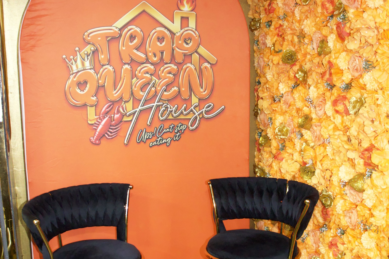 The orange welcome arch with the Trap Queen House logo, a wall of orange flowers and two black and gold bar stools.